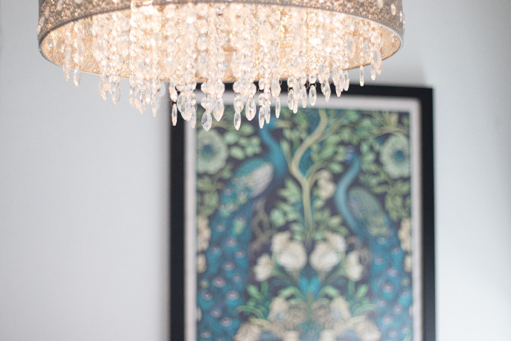 Chandelier hanging over a framed painting of a peacock